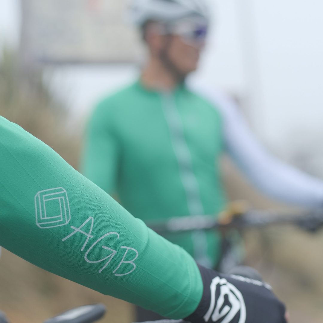 logo que se muestra en la mang y al fondo difuminado un ciclista con el jersey Verde eco A Guapa Bike.